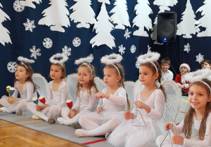 dziewczynki przebrane za aniołki śpiewają i grają na instrumentach