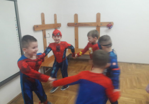 chłopcy w kostiumach super bohaterów tańczą w kole trzymając się za dłonie