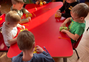 chłopcy siedząc przy stoliku uczą się czyścić szczeliny międzyzębowe, wykorzystują kolorowe klocki zaklejone plasteliną i sznurek