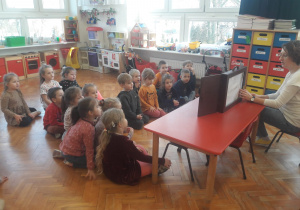 przedszkolaki zgromadzone przed ekranem umieszczonym na stoliku słuchają opowiadania