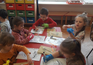 dzieci rysują kolorowymi mazakami zarazki na zębach na kartce z wydrukowaną szczęką