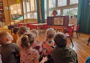 przedszkolaki słuchają opowiadania i oglądają ilustracje do niego na małym ekranie umieszconym na stoliku