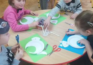 dzieci przy stoliku podczas wykonywania pracy plastycznej - biały kot z papierowego talerzyka