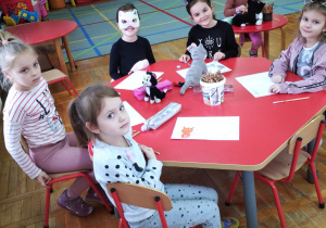 dziewczynki rysują koty a na stoliku siedzą maskotki kotów przyniesione przez dzieci