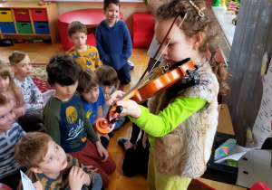 Ania gra na skrzypcach przed dziećmi patrząc na nuty trzymane przez koleżankę