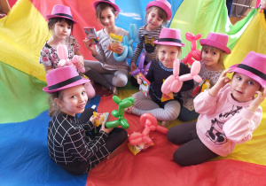 dziewczynki z grupy III w różowych kapeluszach siedzą na kolorowej chuście z upominkami