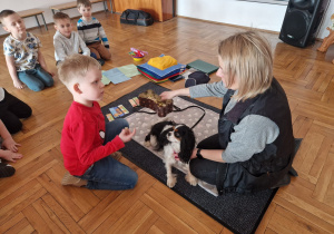 chłopiec trzyma przysmak dla psa i siedzi obok opiekunki z psem Molly