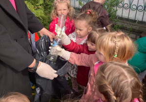 przedszkolaki wrzucają szklane pojemniki do worka ze śmieciami