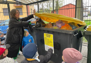 przedszkolaki przyglądają się jak kobieta wyrzuca śmieci do pojemnika