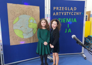 Ania i Zuzia pozują do zdjęcia na tle ddekoracji: narysowanej planety i tytułu przeglądu