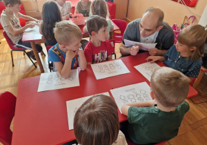 prowadzący warsztaty rozmawia z dziećmi przy stoliku podczas ich pracy na kartkach