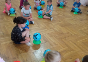 przedszkolaki siedzą w rozsypce z piłkami przed sobą ustawionymi na plastikowych podstawkach