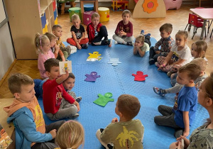 przedszkolaki siedzą w kole z panią psycholog a chłopiec demonstruje obrazek