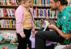 dziewczynka słucha bicia serca kota, który siedzi na kolanach pana weterynarza