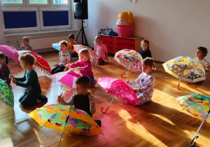 dzieci siedzą za rozłożonymi parasolami i grają na nich drewnianymi pałeczkami