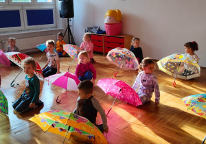dzieci siedzą za rozłożonymi parasolami