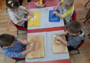 dzieci przy stolikach kroją jabłka na deskach