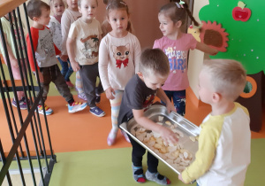 przedszkolaki niosą tacki z jabłkami po przedszkolnym korytarzu do kuchni