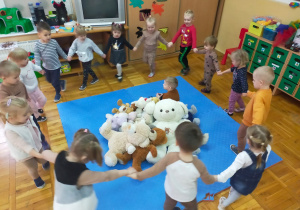 zabawa ruchowa "Stary niedźwiedź mocno śpi" - dzieci trzymają się za ręce i śpiewają idąc wokół chłopca i misiów położonych na środku dywanu