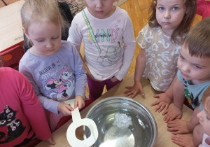 przedszkolaki zgromadzone wokół miski z wodą, pojemnika z woskiem, dziewczynka trzyma papierowy klucz