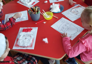 przedszkolaki przy stoliku wykonują podobiznę Mikołaja z wykorzystaniem waty i kolorowego papieru