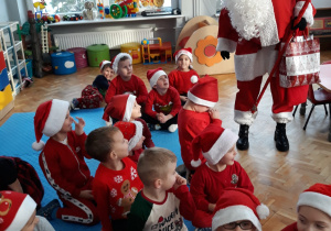 Mikołaj z upominkami stoi wśród dzieci