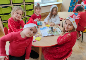 przedszkolaki siedzą przy stoliku w czerwonych ubraniach i czapkach