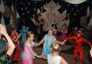 zewnętrzne koło dzieci z nauczycielką klaszczą w dłonie a dziewczynki w środku tańczą w kółku