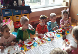 dzieci siedzą przy długim stoliku podczas poczęstunku