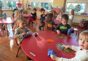 przedszkolaki przy stolikach wkładają do gumowych rękawiczek różne materiały