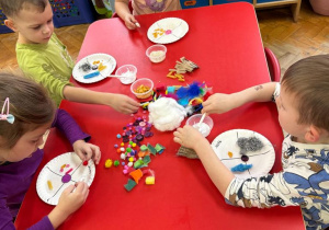 przedszkolaki przy stolikach wybierają różne materiały i naklejają je na talerzyki tekturowe