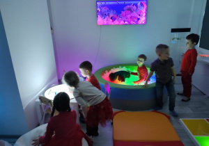 przedszkolaki w sali doświadczania świata przy podświetlanym stoliku i w podświetlanym basenie z kulkami