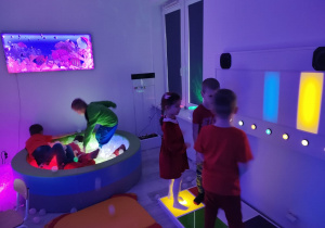 przedszkolaki w sali doświadczania świata w podświetlanym basenie a obok dzieci wydobywają dżwięki