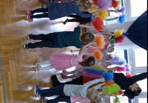 przedszkolaki stoją w gromadce obok pani Nutki z rękami uniesionymi w górę, w których trzymają kolorowe pompony