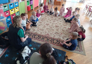 dzieci siedzą w kole na dywanie wraz z instruktorkami i psami