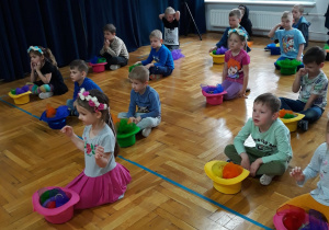 dzieci siedzą przed kolorowymi kapeluszami wypełnionymi kolorowymi chustami