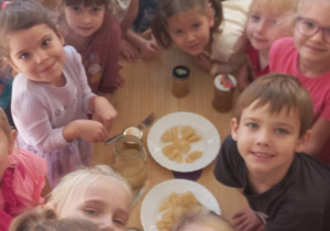 dzieci wrzucają pokrojone jabłka do słoika i zalewają wodą robiąc kompot