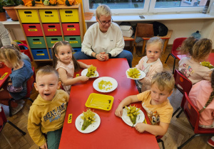 przedszkolaki przy stoliku z mamą podczas wykonywania owocowego jeżyka z winogrona i gruszki