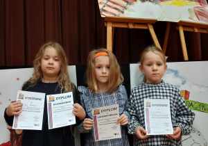 trzy dziewczynki biorące udział w konkursie z dyplomami