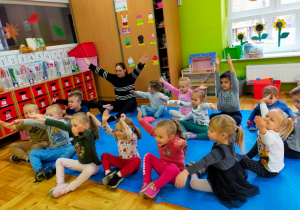 przedszkolaki wraz z panią Kasią siedzą na dywanie i podnoszą dłonie