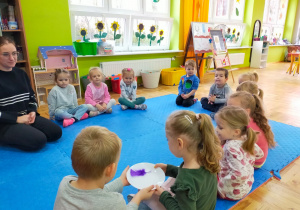 dzieci siedzą w kole i przekazują sobie kolejno talerzyk z piórkiem