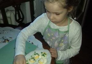 dziewczynka w fartuszku z talerzem jajek przekrojonych na pół, posmarowanych majonezem i posypanych szczypiorkiem
