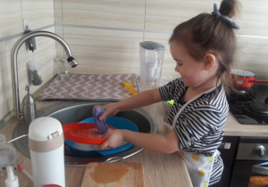 dziewczynka stoi w kuchni i zmywa naczynia
