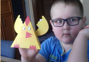 chłopiec w okularach pokazuje kurczaka wykonanego z papieru
