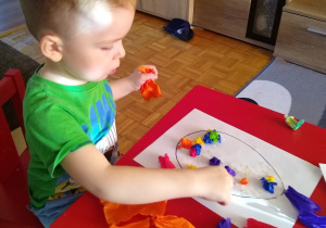 dziecko wykleja kolorową bibułą kontur jajka