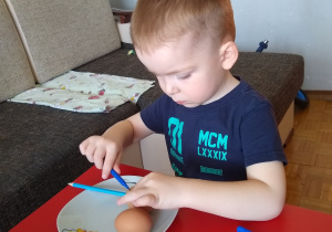 chłopiec maluje pisanki mazakami