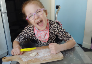 dziewczynka kroi nożem ciasto na drewnianej desce