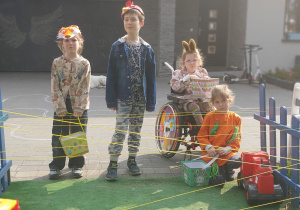 czwórka dzieci stoi przed domem z koszyczkami a przed nimi labirynt z żółtych nitek