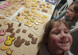 dziewczynki ozdabiają lukrem żółtym i różowym ciasteczka w kształcie głowy zajączka