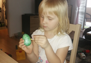 dziewczynka maluje zielone jajko patyczkiem do ucha, maczanym w kolorze żółtym